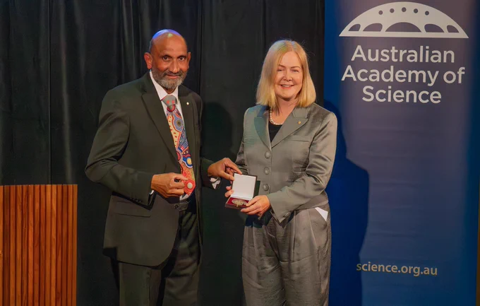 An individual receives an award from another individual at an Australian Academy of Science event.