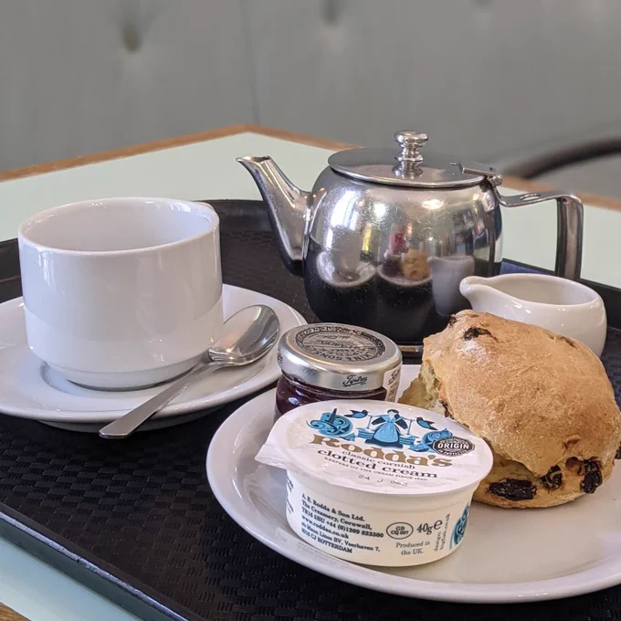 Scone, cream, jam, tea cup, milk jug and teapot on a black tray