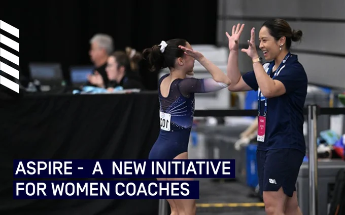 Two gymnasts celebrating with a high-five at an event, with the text "ASPIRE - A NEW INITIATIVE FOR WOMEN COACHES" displayed.