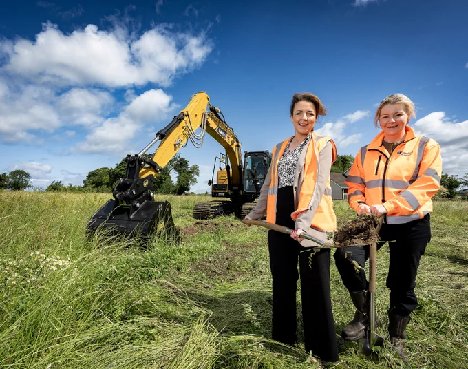 Photo taken on site of Minister & Translink Representative with a digger in the background & minister holding a spade, with soil on it. 