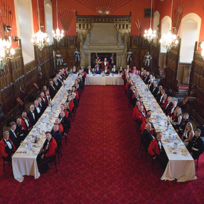 Guests seated at a formal banquet in the Great Hall at Edinburgh Castle, with elegant red carpeting and historic architectural details visible.
