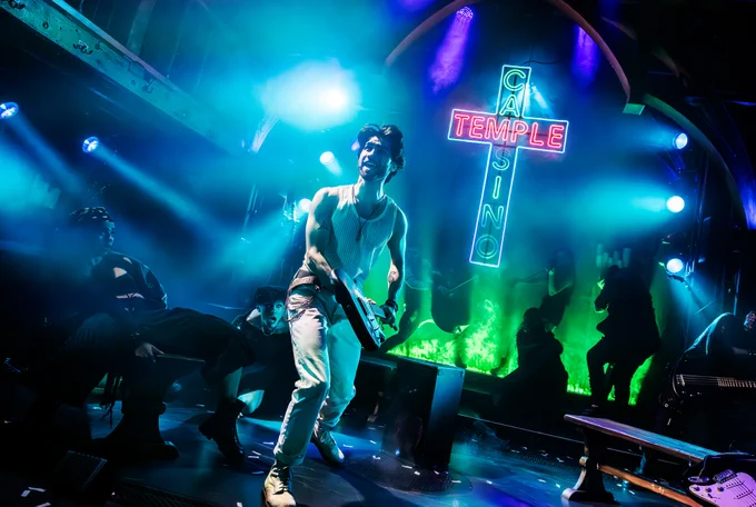 A photo showing a man in a vest performing in a theatre made to look like a neon-lit temple 
