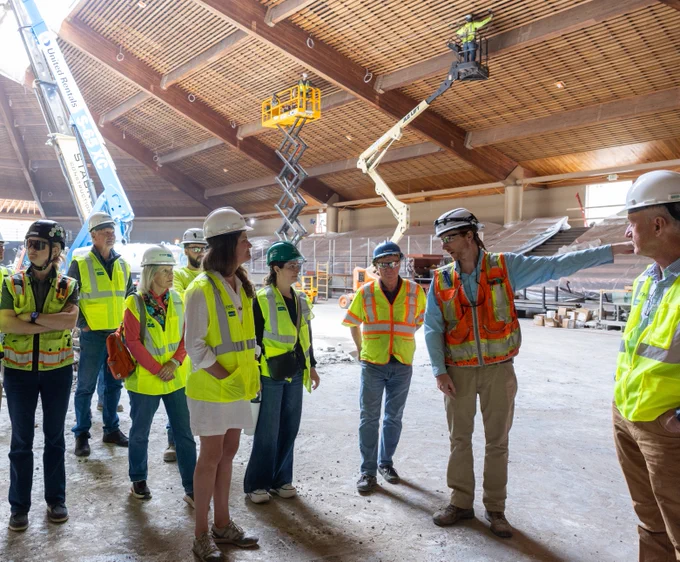 Vail Town Council and others in safety gear having a discussion at a construction site, with cranes and building materials visible in the background.