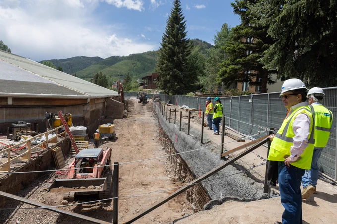 Vail Town Council and others in safety vests at a building site with excavation work in progress, surrounded by natural scenery.