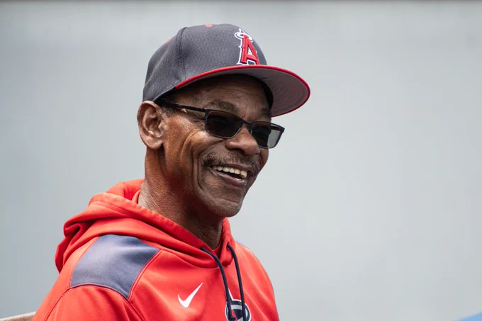 Ron Washington smiles in a candid photo. He is wearing a red Los Angeles Angels sweatshirt and a dark blue Angels cap.