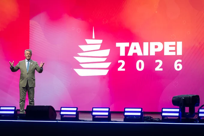 Person standing on stage at the 2025 Rotary International Convention, gesturing while speaking, with a large logo and 'TAIPEI 2026' text in the background.