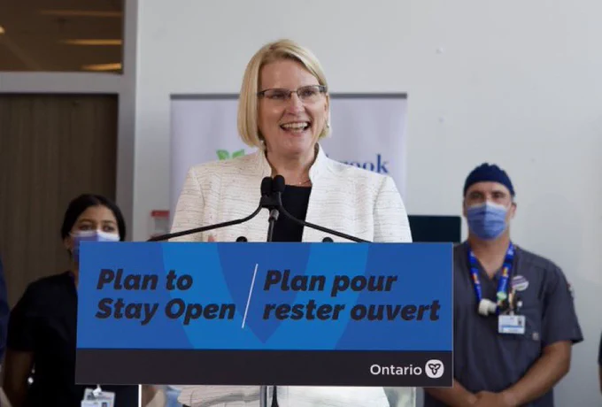 A picture of Sylvia jones at a podium with a sign that says ‘plan to stay open’
