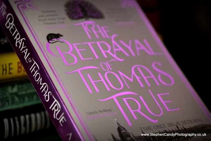 The cover of paperback of "The Betrayal of Thomas True" with shiny foil effects.