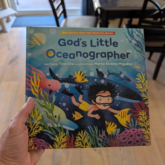 Cover of God's Little Oceanographer by Tina Cho features a child swimming in the ocean with a dolphin, squid, whale shark, coral, and more.