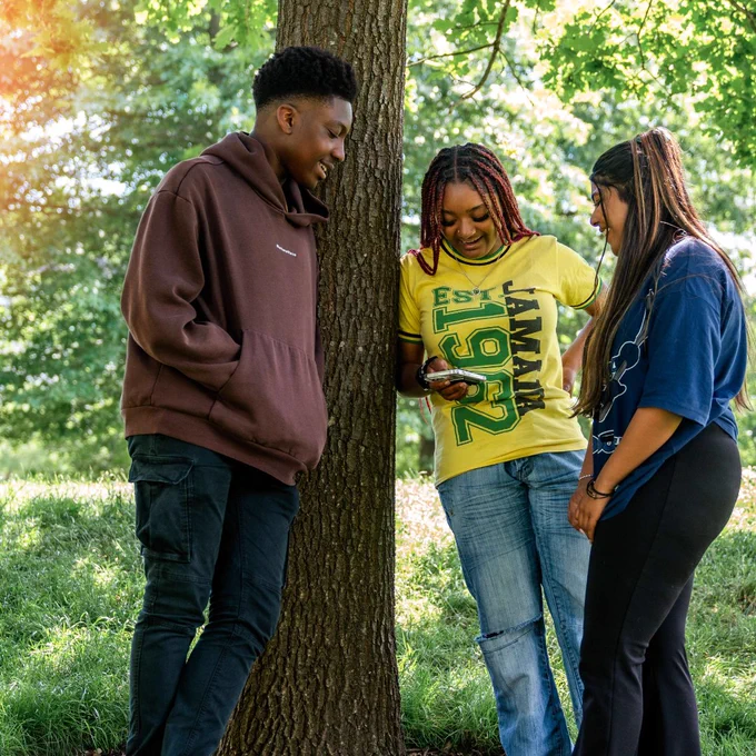 three young people stood at a tree, looking down at their phones smiling