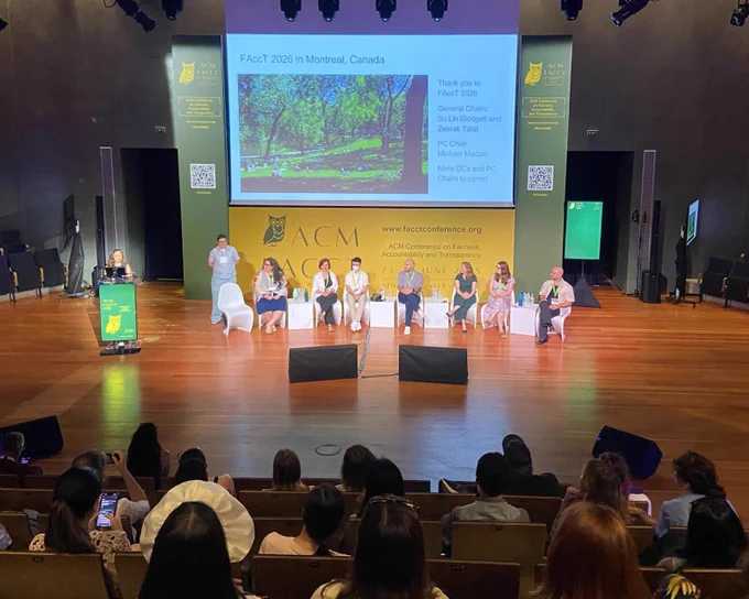 Photo of the Town Hall meeting at last week's conference. The audience watches as Su Lin Blodgett announces the location of next year's conference. Su Lin Blodgett and Zeerak Talat will be General Chairs, and Michael Madaio will be PC Chair.