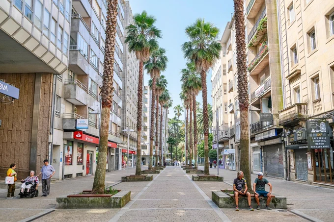 People of all ages and abilities walk, cycle, sit, and socialise on the car-free streets of Pontevedra, which are lined with buildings, trees, benches, and patios.