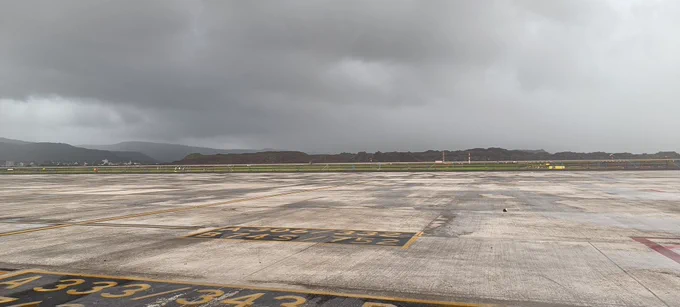 Dark clouds above hills, and in foreground taxiway and runway waiting for rains
