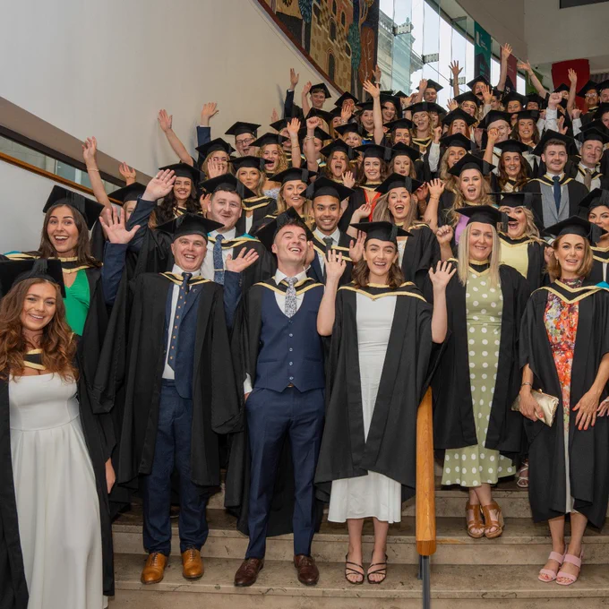 The first cohort of Ulster University School of Medicine Graduates on the steps inside the Millenium Forum, raising their hands and cheering.