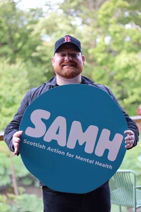 Cammy Barnes smiles holding a SAMH logo
