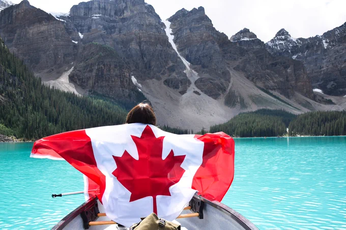 Person in a canoe holding Canadian flag, surrounded by turquoise lake and mountains 
