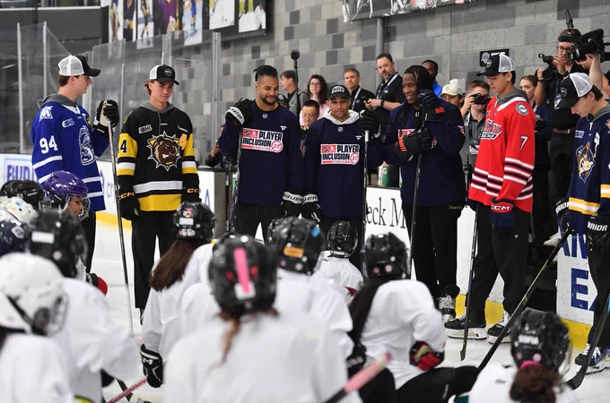 Photo of group of people talking to players on ice, including Porter Martone, Simon Wang, and Jake O'Brien
