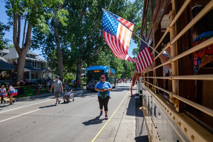 American flags wave out the windows of a trolley in a parade