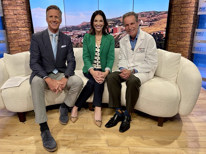 FOX13 Good Day Utah anchors, Dan Evans and Kelly Chapman, sit next to MountainStar Healthcare Chief Medical Officer, Dr. Filip Roos, on set, smiling.