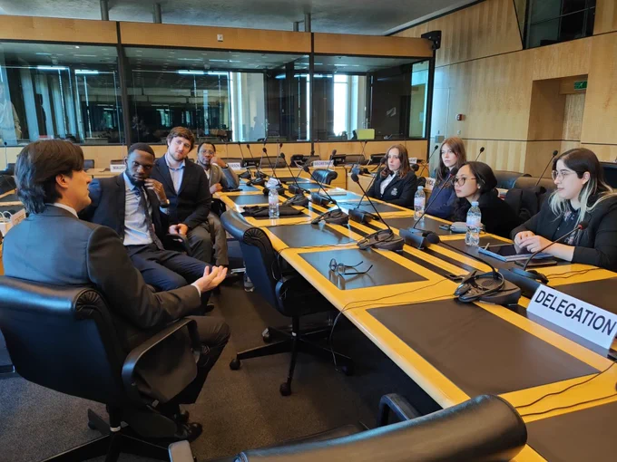 A group of people sat talking in a board room. On the table is the sign delegation.