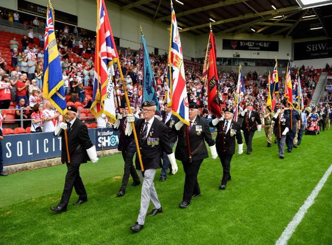 Armed Forces Community marching through Saints' Totally Wicked Stadium with flags for Armed Forces Day celebrations