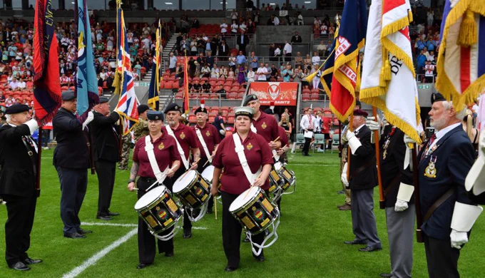 Drummers marching on the pitch at Saints' Totally Wicked Stadium with Armed Forces Community either side holding flags as part of Armed Forces Day celebrations