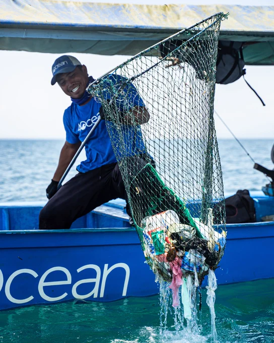 4ocean worker lifting a fishing net full of plastic from the ocean aboard a boat labeled "4ocean"