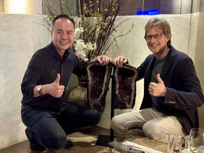 Jack Huynh and Mark Cerny side by side, smiling and giving thumbs up, each touching a piece of amethyst split from the same stone — symbolizing their friendship and the co-engineered partnership behind Project Amethyst.