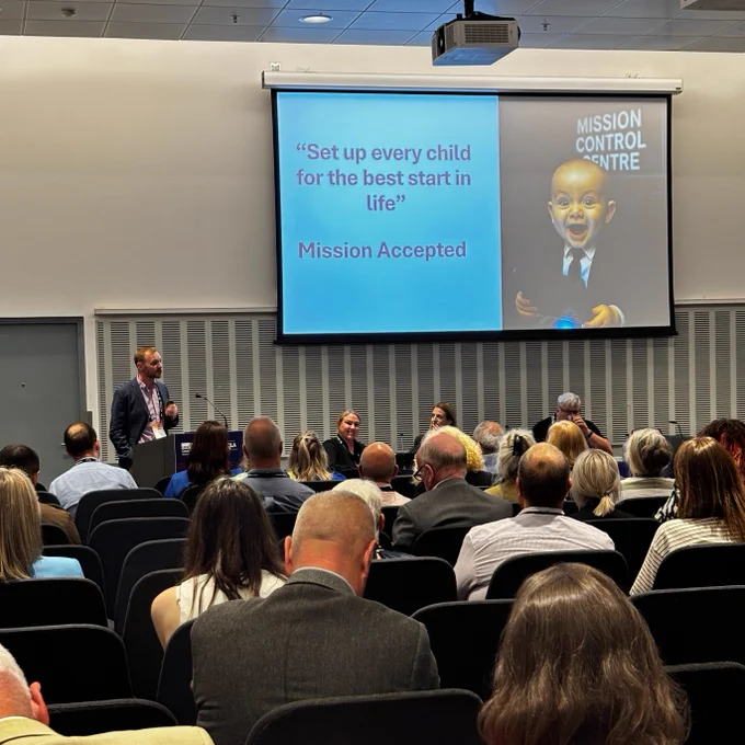 A busy session with packed chairs and a large screen