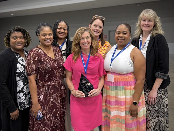 Hope Seeley holding her award and standing beside Melissa Lindsey, Emily Elam, and other HCS and event representatives