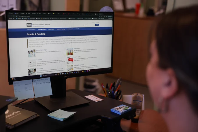 A desktop is open to the NIH's page on grants and funding.