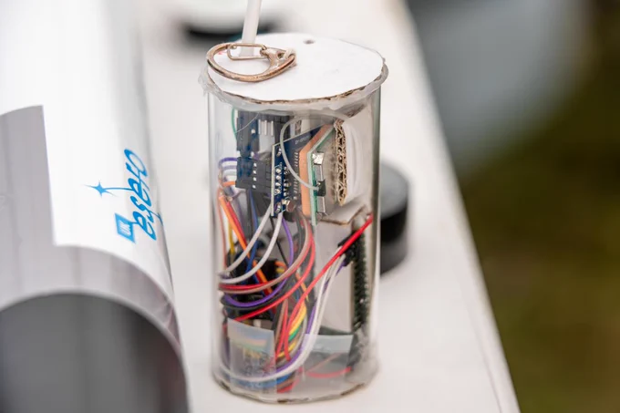 Clear cylindrical container displaying electronic components and wires, mounted on a surface with a logo reading "ESERO".