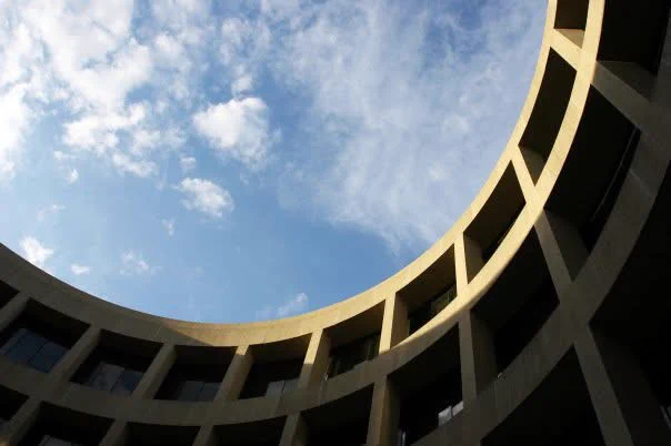 View of the curved exterior of the Hirshhorn Museum, with a partly cloudy sky in the background.