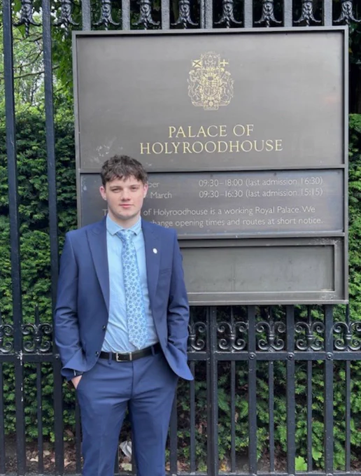 Former pupil Charlie Munro standing in front of a sign outside the Palace of Holyrood.