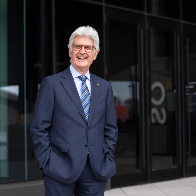A person in a business suit smiling in front of a building with glass doors.