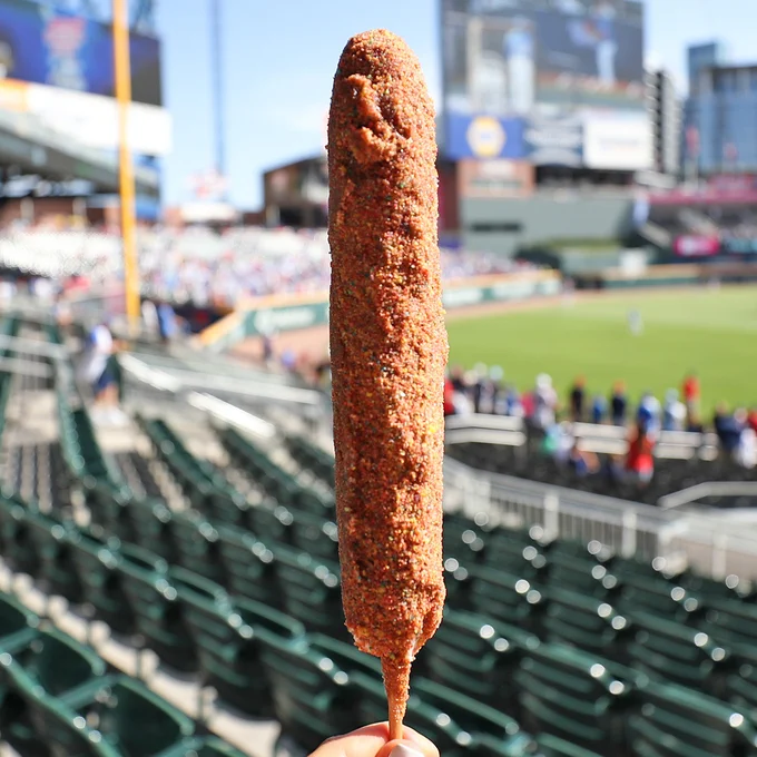 A deep fried hot dog on a stick in front of a backdrop of Truist Park