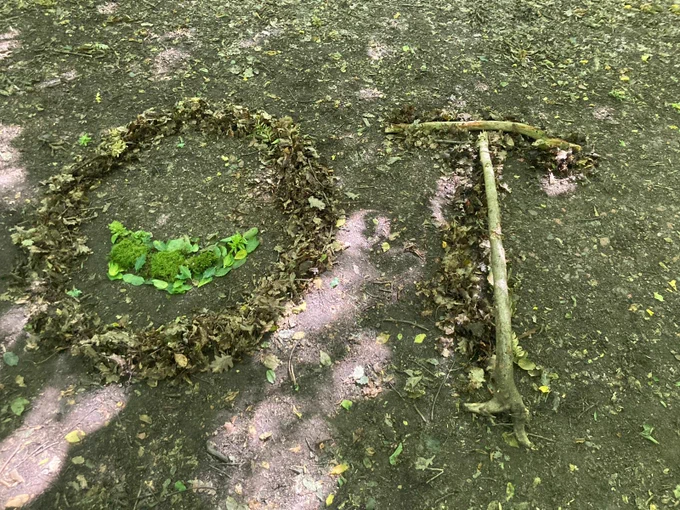 Leaves and twigs arranged to form the letters O and T on a woodland floor.