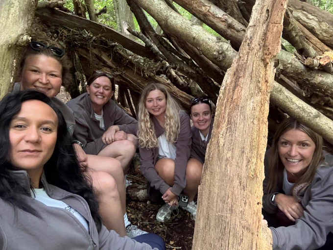 A group of six women sitting in a den made of tree branches.