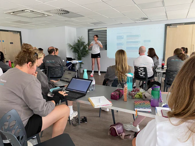 A woman giving a presentation to a room full of colleagues.