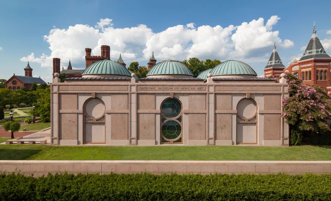 Front exterior view of the National Museum of American Art featuring a symmetric facade with three round domes and a central green door, set against a clear sky.