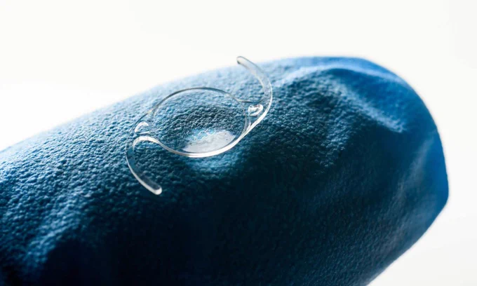 Close up of an intraocular lens on the finger of a gloved hand. 