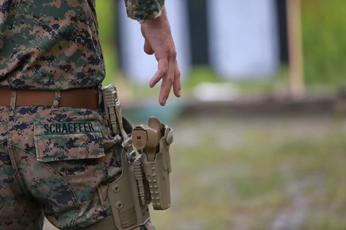 Close-up of Marine’s holstered pistol and hand reaching toward it during weapons training.