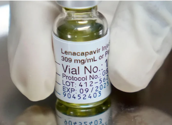 Close-up of a gloved hand holding a vial labelled Lenacapavir Injection with dosage and expiration details visible.