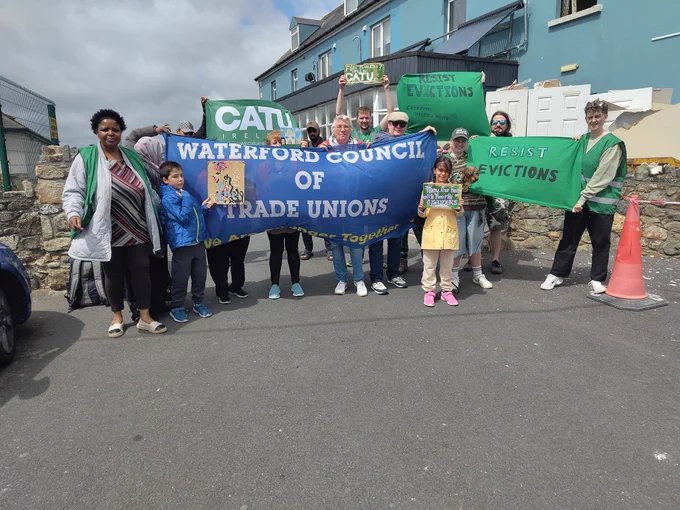 Another photo of CATU members, residents, and locals holding up signs and flags.