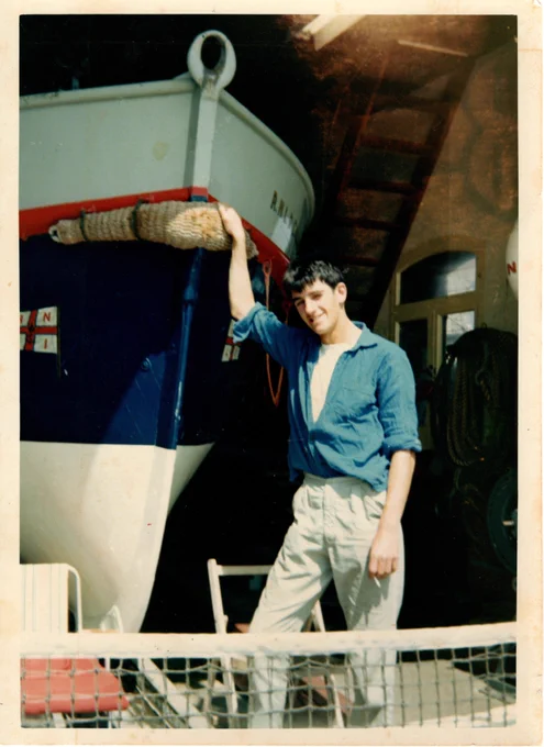 Richard Spindler stands in front of an RNLI lifeboat holding the hull in a boat shed. The setting includes visible tools and equipment around, suggesting maintenance work.