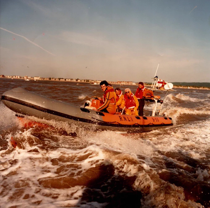 Three RNLI crew members manoeuvre a speedy lifeboat on choppy sea waters.