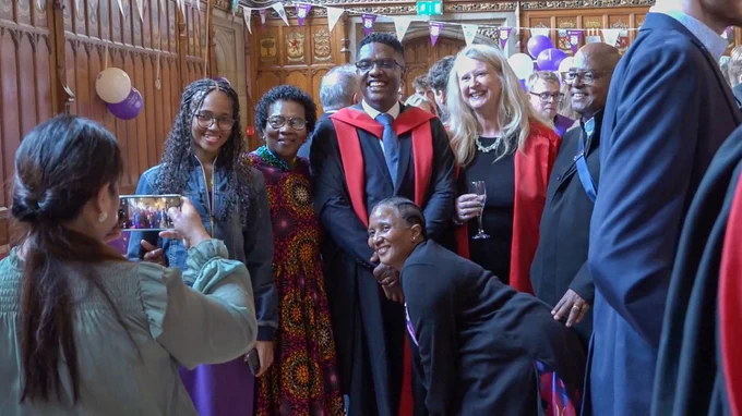 Colour photo of a person taking a photo of a group of people posing together.
