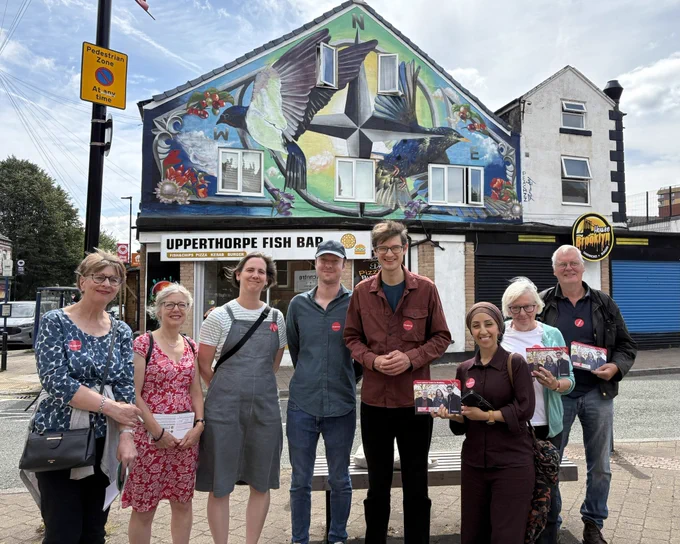 A photo of eight people standing in front of Upperthorpe Fish Bar in Upperthorpe. The building had a large mural on the side of it