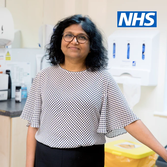 A photograph of a GP standing in their surgery. They are smiling at the camera. 