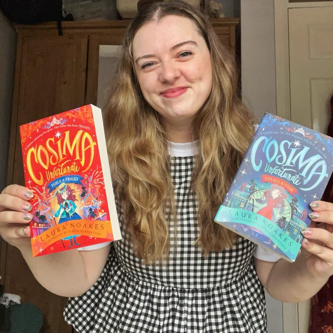 Laura, a white woman with long blonde hair is wearing a gingham blouse and smiling at the camera, holding up two of her books: Cosima Unfortunate Steals a Star and Cosima Unfortunate Foils a Fraud.